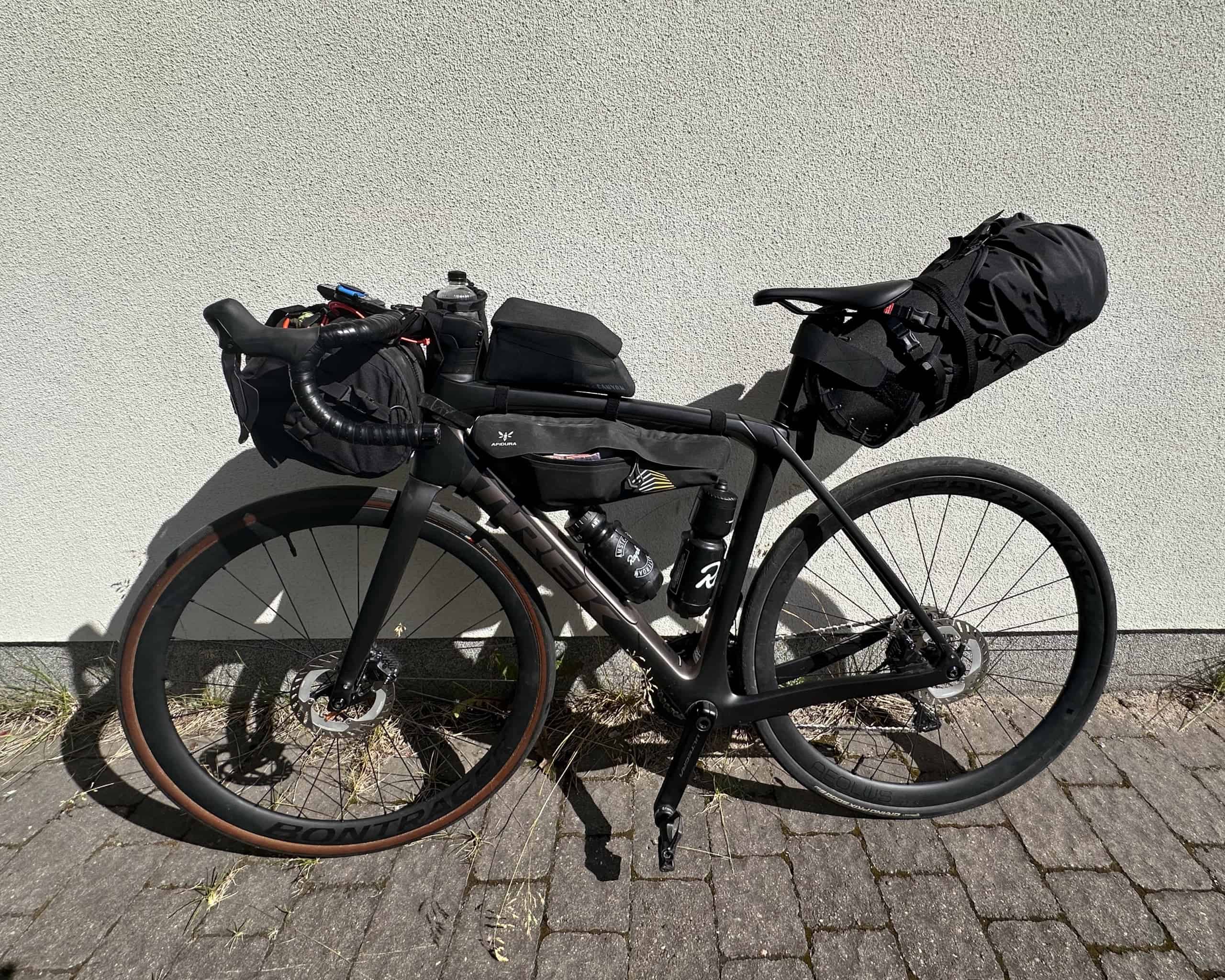 Trek Domane SL7 -maantiepyörä matkavarustuksessa nojaamassa valkoiseen seinään.