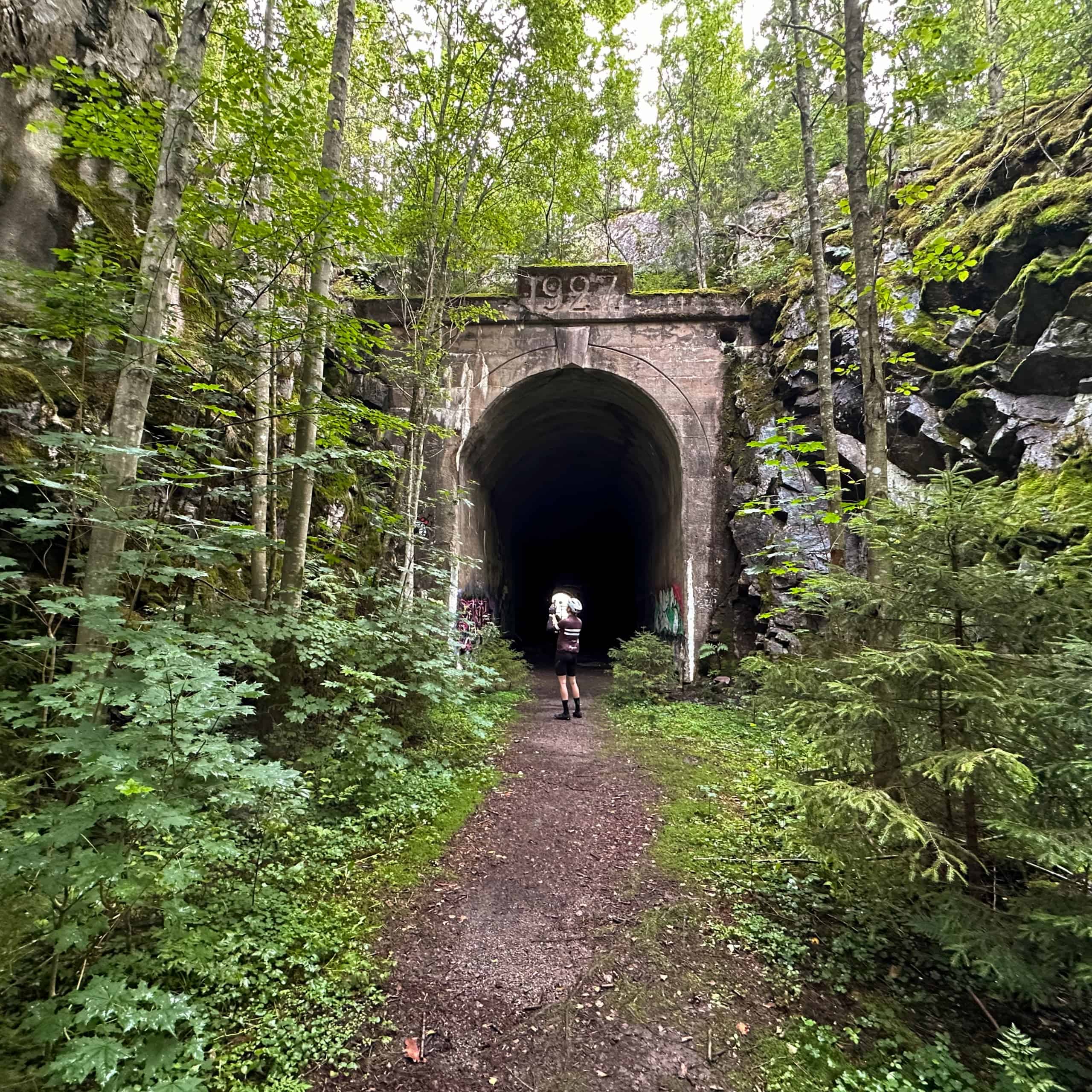 Halikon vanha rautatietunneli vehreän kasvillisuuden keskellä, tunnelin edessä pyöräilijä.